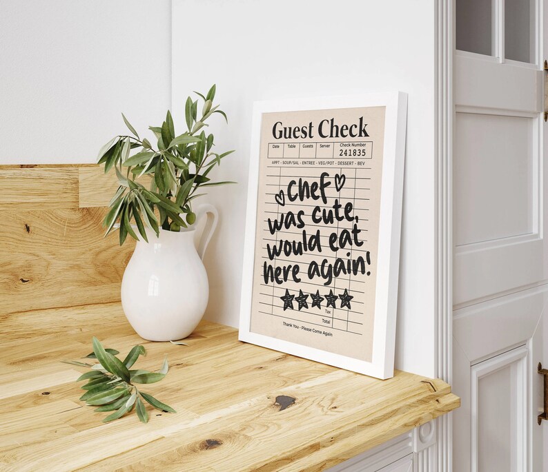 May include: A framed guest check with a handwritten message that reads "Chef was cute, would eat here again!" with five stars for a rating. The check is on a light brown background with black lines and text.