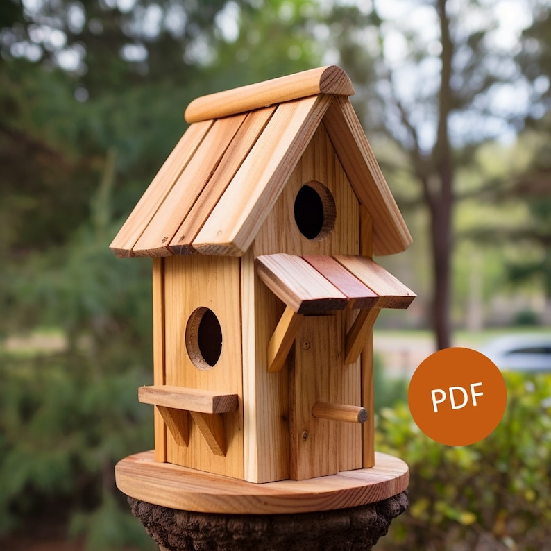 May include: A wooden birdhouse with a shingled roof and two nesting compartments. The birdhouse is painted in a natural wood color and has a small perch on the front. The birdhouse is sitting on a wooden base.