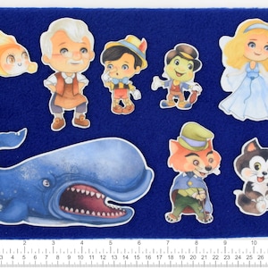 Könnte beinhalten: Ein blauer Filz-Brett mit verschiedenen bunten Filz-Ausschnitten von Figuren aus klassischen Kindergeschichten. Die Figuren sind Pinocchio, Geppetto, ein blauer Wal, eine Fee, ein Fuchs, eine Katze und ein Frosch.
