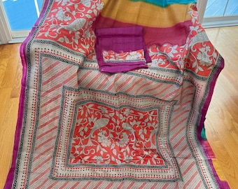 May include: A cream-colored saree with a pink border and tassels. The saree has a multi-colored striped pattern on one end and a floral print on the other end. The floral print features red, white, and black colors.