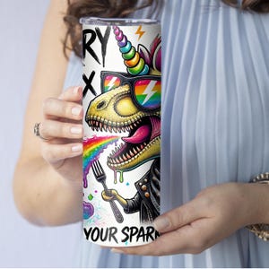 Puede incluir: Un vaso de acero inoxidable blanco con una ilustraci&oacute;n colorida de un dinosaurio unicornio con gafas de sol y comiendo un arco&iacute;ris. El texto "Sorry Not Sorry" y "Your Spark" est&aacute; impreso en el vaso.