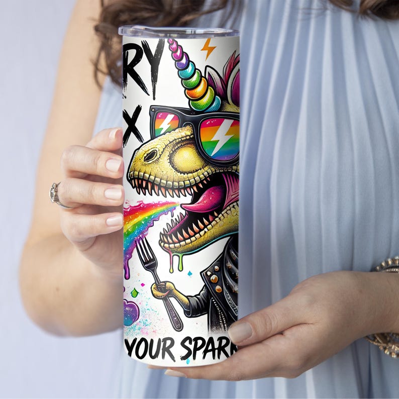 Puede incluir: Un vaso de acero inoxidable blanco con una ilustraci&oacute;n colorida de un dinosaurio unicornio con gafas de sol y comiendo un arco&iacute;ris. El texto "Sorry Not Sorry" y "Your Spark" est&aacute; impreso en el vaso.