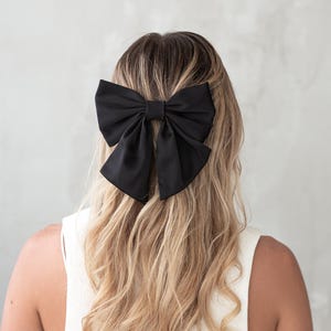 May include: A large black satin bow hair clip. The bow is tied in a large, full knot and is secured with a clip.