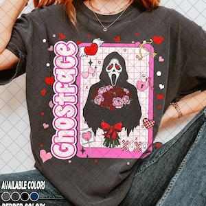 May include: Dark gray t-shirt featuring a graphic of the Ghostface character holding a bouquet of red roses, surrounded by hearts and the word "Ghostface" in pink. The design includes a pink frame with a grid pattern and the text "XOXO".