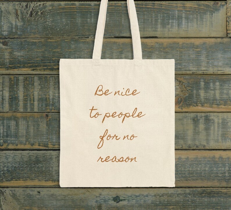 May include: A white tote bag with brown text that reads "Be nice to people for no reason".