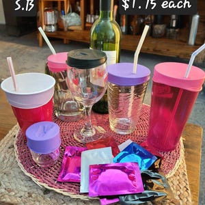 May include: A set of six colorful reusable drink lids with straws, a wine bottle, and six small packets of drink mix. The lids are pink, purple, and black. The packets are red, white, blue, pink, and black. The text "$1.75 each" is visible in the image.