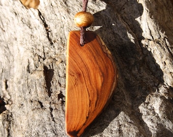 May include: A wooden pendant necklace with a brown cord and a wooden bead. The pendant is a light brown color with dark brown streaks and a curved shape.