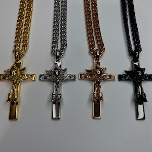 May include: Four cross necklaces in gold, silver, rose gold, and black. Each pendant features a detailed figure on the cross, suspended from a matching chain. The necklaces are displayed against a plain background, highlighting the jewelry.