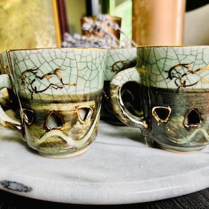 May include: Set of four ceramic espresso cups with a crackle glaze in shades of green and brown. Each cup features a gold rim and a gold illustration of a running horse. The cups have decorative cutouts and are displayed on a marble tray.