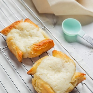 May include: Two golden brown pastries with a white cream filling on a silver wire rack. The pastries are shaped like stars.