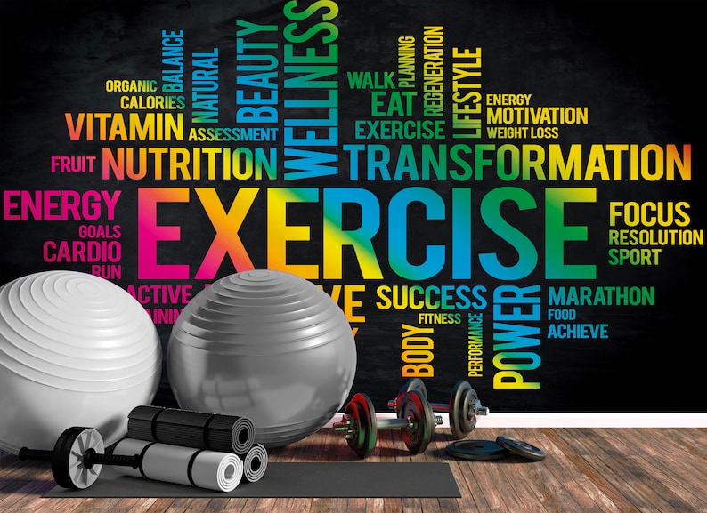 May include: A black chalkboard with colorful text about fitness and exercise. The text includes words like "exercise", "transformation", "wellness", "nutrition", "energy", "motivation", "success", "power", "marathon", "achieve", "focus", "resolution", "sport", "body", "fitness", "goals", "cardio", "run", "active", "walk", "planning", "regeneration", "lifestyle", "eat", "organic", "balance", "natural", "beauty", "calories", "vitamin", "assessment", "fruit", "weight loss". There are two exercise balls, one white and one gray, and a set of dumbbells on a black yoga mat.