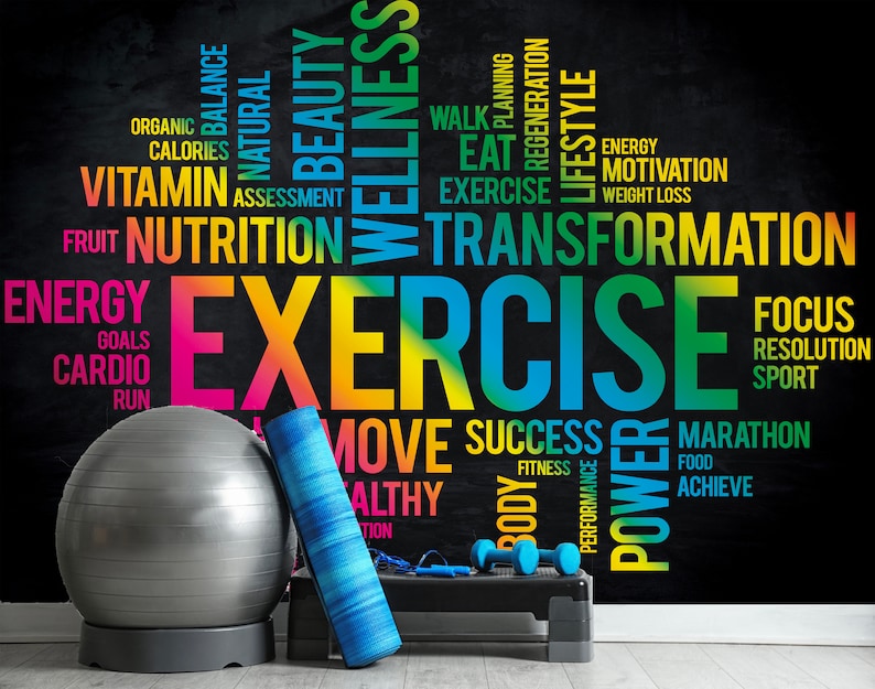 May include: A black chalkboard with colorful text about fitness and wellness. The text includes words like "exercise", "transformation", "nutrition", "energy", "goals", "cardio", "run", "move", "success", "power", "marathon", "achieve", "focus", "resolution", "sport", "fitness", "body", "performance", "food", "organic", "balance", "natural", "beauty", "wellness", "calories", "vitamin", "assessment", "fruit", "planning", "regeneration", "lifestyle", "walk", "eat", "motivation", "weight loss". There is a gray exercise ball, a blue yoga mat, and a black step platform with dumbbells on it in the foreground.