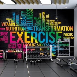 May include: A black chalkboard wall with a colorful word cloud centered around the word "EXERCISE". The word cloud includes words related to fitness, health, and wellness. The wall is in a gym setting with weight racks and other fitness equipment.
