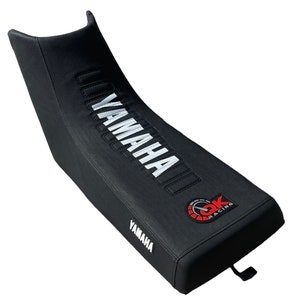 Puede incluir: Funda de asiento de moto negra con la inscripción "YAMAHA" en blanco y un logotipo "GK Racing" rojo y negro.