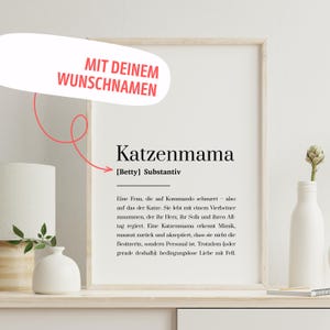 Könnte beinhalten: Gerahmter Druck mit dem Wort "Katzenmama" und dem Namen "Betty" darunter. Der Text ist schwarz auf weißem Hintergrund. Oben im Rahmen befindet sich ein rotes Banner mit der Aufschrift "MIT DEINEM WUNSCHNAMEN".