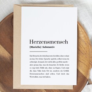 Könnte beinhalten: Eine weiße, rechteckige Grußkarte mit dem Wort Herzensmensch in fetter schwarzer Schrift, gefolgt von einer Definition in deutscher Sprache. Die Karte steckt in einem hellbraunen Kraftpapier-Umschlag und zeigt ein schlichtes Design.