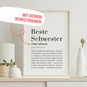Könnte beinhalten: Ein gerahmter Druck mit den Worten "Beste Schwester" in großen schwarzen Buchstaben, was "Beste Schwester" bedeutet. Der Druck enthält einen Platz für einen individuellen Namen und eine Definition. Eine weiße Vase mit einer Blume und eine kleine weiße Vase im Vordergrund.