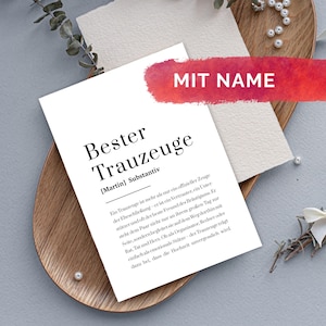 Könnte beinhalten: Eine weiße Karte mit dem Text "Bester Trauzeuge" in Schwarz, darunter der Name "Martin". Ein rotes Banner mit "MIT NAME" befindet sich oben. Die Karte liegt auf einem Holztablett mit dekorativen Elementen.