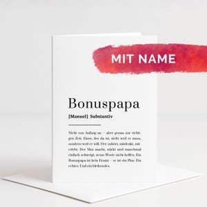 Könnte beinhalten: Eine weiße Grußkarte mit dem Wort Bonuspapa, definiert als Substantiv mit dem Namen Manuel in Klammern. Über dem Text befindet sich ein roter Aquarell-Pinselstrich mit dem weißen Text MIT NAME. Die Karte ist gefaltet und steht aufrecht.