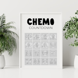 May include: A framed print with the words "CHEMO COUNTDOWN" in bold black letters. Below, a grid of inspirational phrases in German, such as "Every day brings you closer to your goal." The print is in a white frame.