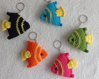 May include: Five crocheted fish keychains in different colors, including black, blue, green, orange, and pink. Each fish has yellow fins and a black eye.