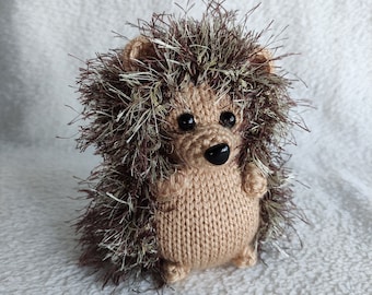 May include: A brown and beige knitted hedgehog toy with black eyes and a black nose. The hedgehog has a brown and white fluffy mane.