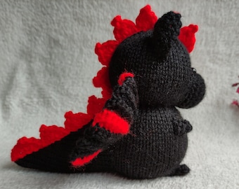 Puede incluir: Un juguete de dragón de punto negro y rojo con una cresta roja puntiaguda y una cola larga.