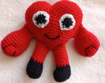 May include: A red crocheted heart-shaped plush toy with black eyes, a white smile, and black feet.