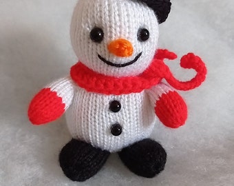 Puede incluir: Un muñeco de nieve de punto blanco con un sombrero negro, una bufanda roja y botones negros. El muñeco de nieve tiene una nariz de zanahoria y ojos negros.