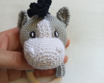 Puede incluir: Un sonajero de bebé hecho a mano en forma de cabeza de burro. El burro tiene un cuerpo gris, hocico blanco y melena negra. Cuenta con un anillo de madera para facilitar el agarre y está diseñado para bebés.