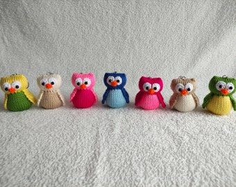 Puede incluir: Una fila de ocho llaveros de búho tejidos en varios colores, incluyendo verde, amarillo, beige, rosa, azul y marrón. Los búhos tienen ojos blancos y picos negros.