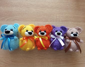 May include: Five colorful, knitted teddy bears in a row. Each bear has a different color: blue, yellow, orange, purple, and tan. They have black noses and white muzzles, and each bear has a ribbon bow.