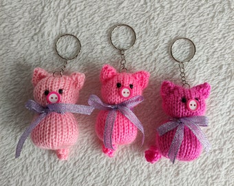 May include: Three pink knitted pig keychains with purple ribbon bows and silver key rings.