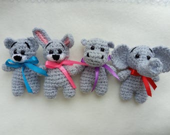 Puede incluir: Cuatro animales de peluche tejidos a crochet: un oso con una cinta azul, un conejito con una cinta rosa, un hipopótamo con una cinta morada y un elefante con una cinta roja. Todos son grises y tienen ojos negros.