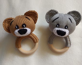 May include: Two knitted bear-shaped baby rattles. One is brown, the other is gray. Each has a white muzzle, black eyes, and a wooden ring. The bears are designed with large ears and are suitable for babies.