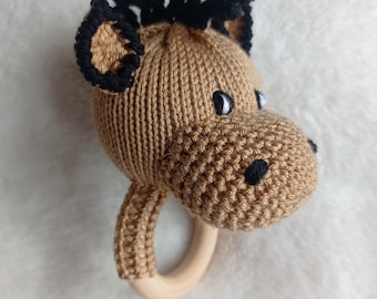 May include: A brown knitted animal rattle with a wooden ring. The animal has black yarn for hair and black embroidered eyes and nose.