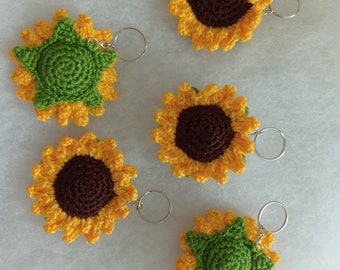 May include: Five crocheted sunflower keychains with silver key rings. The sunflowers are yellow with brown centers and some have green leaves.