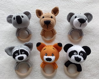 Puede incluir: Seis juguetes de sonajero de animales de punto con anillos de madera. Los animales son un koala, un perro, un oso, un mapache, un zorro y un panda. Los juguetes son todos grises, marrones, naranjas y negros.