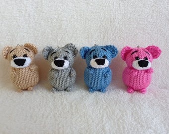 May include: Four knitted teddy bears in different colors: beige, gray, blue, and pink. Each bear has a black nose and eyes.