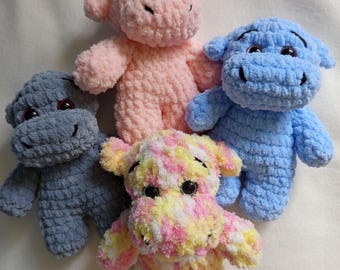 May include: A collection of five handmade crochet hippo plushies in various colors. The plushies are in shades of pink, blue, gray, and a multi-colored mix of pink, yellow, and white. Each hippo has small, black eyes and a smiling expression.