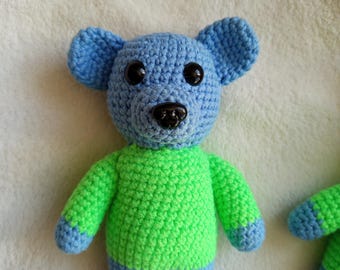 May include: A crocheted blue and green teddy bear with black eyes and a black nose.