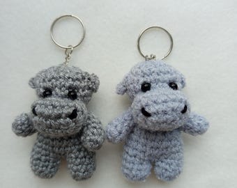 May include: Two gray crocheted hippopotamus keychains with black eyes and a silver key ring.