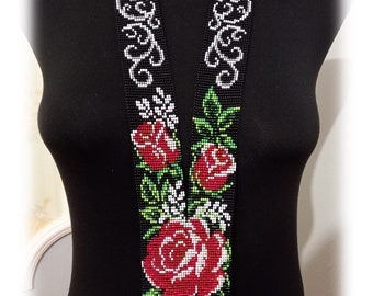 May include: A black beaded necklace with a white and black floral design and red roses. The necklace has a fringe at the bottom.