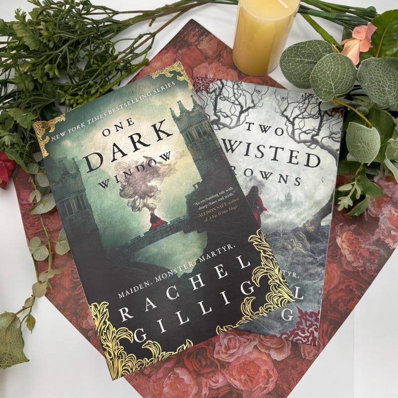 May include: Two fantasy novels, "One Dark Window" and "Two Twisted Crowns", by Rachel Gillig. The covers feature dark, moody illustrations with gold accents.