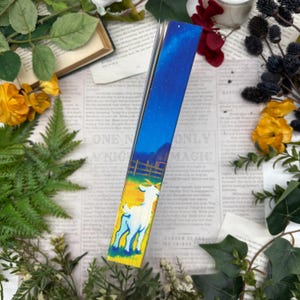 Puede incluir: Marcapáginas con una ilustración de una cabra en un campo bajo un cielo estrellado. El marcapáginas presenta un degradado de colores, del amarillo al azul. El texto "ONLY MAGIC" es visible.