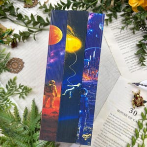Może przedstawiać: Trzy książki z ozdobnymi krawędziami stron z ilustracjami o tematyce kosmicznej. Pierwsza przedstawia astronautę na czerwonej planecie, druga astronautę unoszącego się w kosmosie, a trzecia futurystyczne miasto pod rozgwieżdżonym niebem.