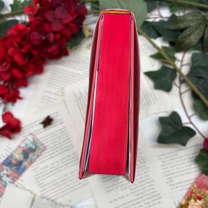 May include: The spine of a red hardcover book with a thin yellow line at the top.