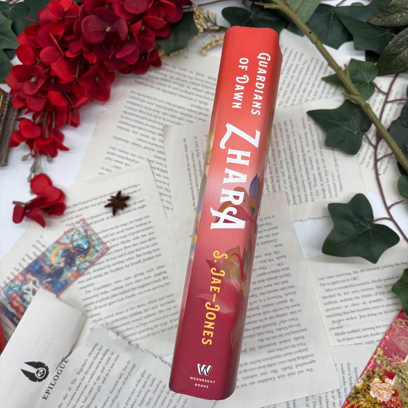 May include: A red hardcover book with the title "Zhara" and the text "Guardians of Dawn" on the spine. The author's name, S. Jae-Jones, is printed below the title. The book is part of the Wednesday Books series.