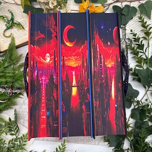 May include: Three hardcover books with matching covers featuring a futuristic cityscape under a red and orange sky with a crescent moon. The spines are red and blue. The books are held together with a purple handle.