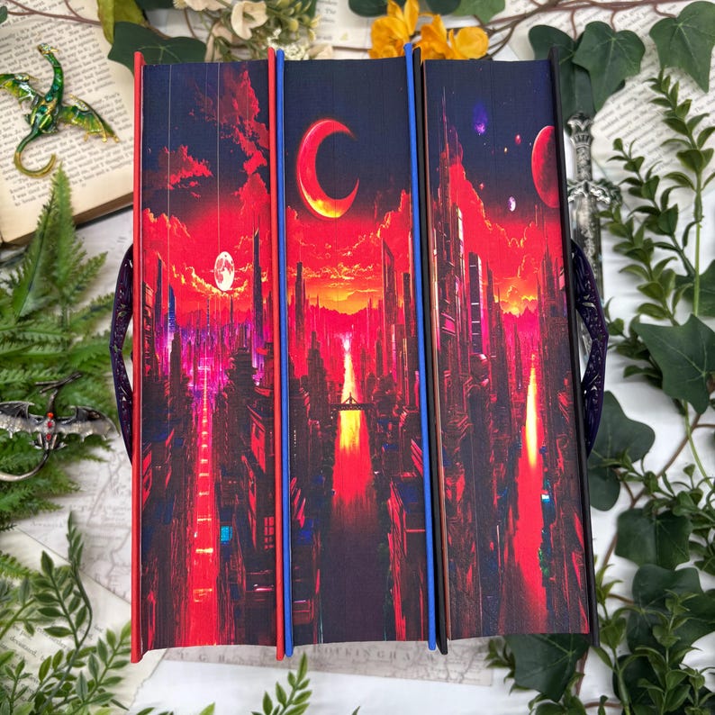May include: Three hardcover books with matching covers featuring a futuristic cityscape under a red and orange sky with a crescent moon. The spines are red and blue. The books are held together with a purple handle.